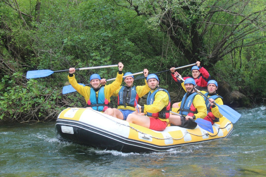 Group of rafters in helmets and life jackets posing in an inflatable raft on the Cetina River