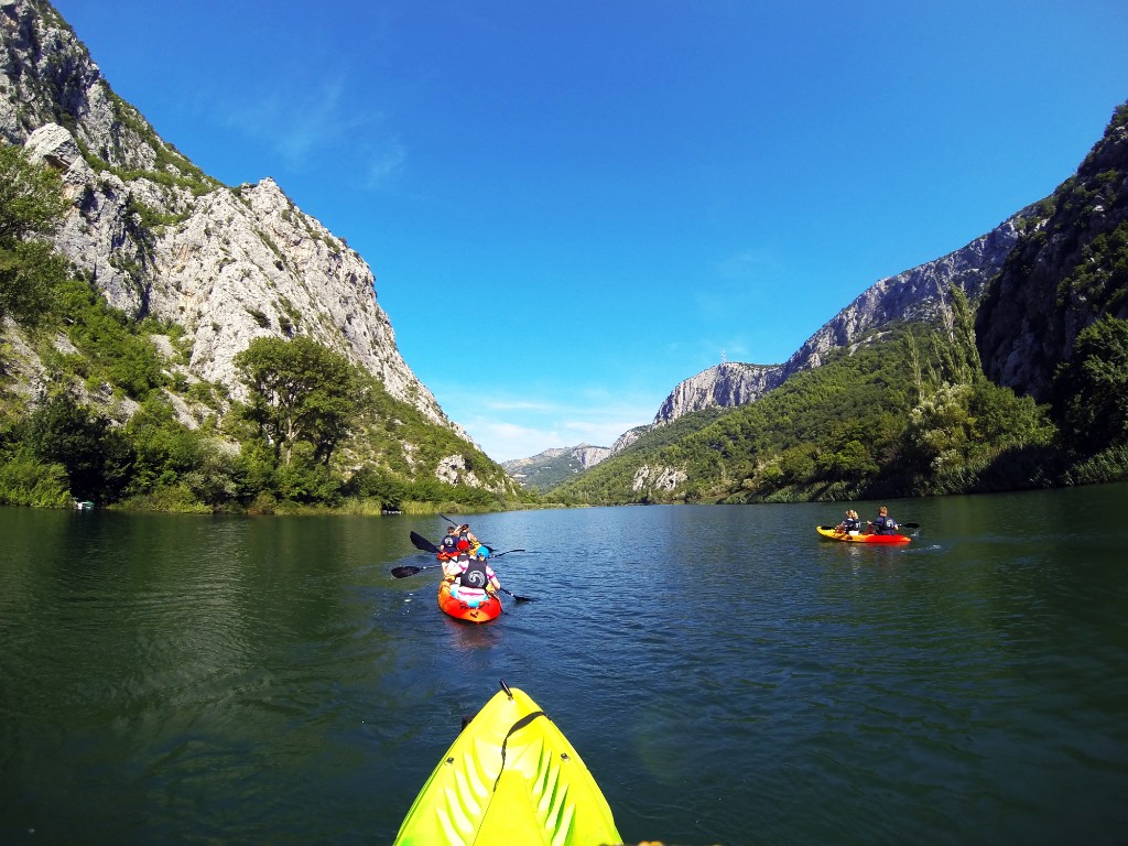 Kayakers paddling on the Cetina River between limestone cliffs under a clear blue sky